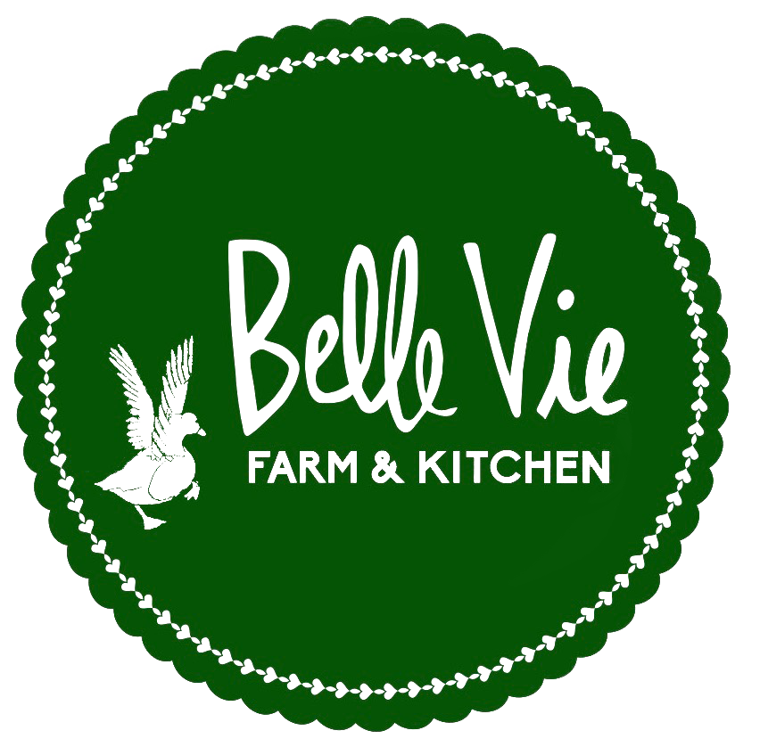 Logo of Belle Vie Farm & Kitchen featuring a green circular design with white text and an illustration of a bird, representing a farm-to-table dining experience.