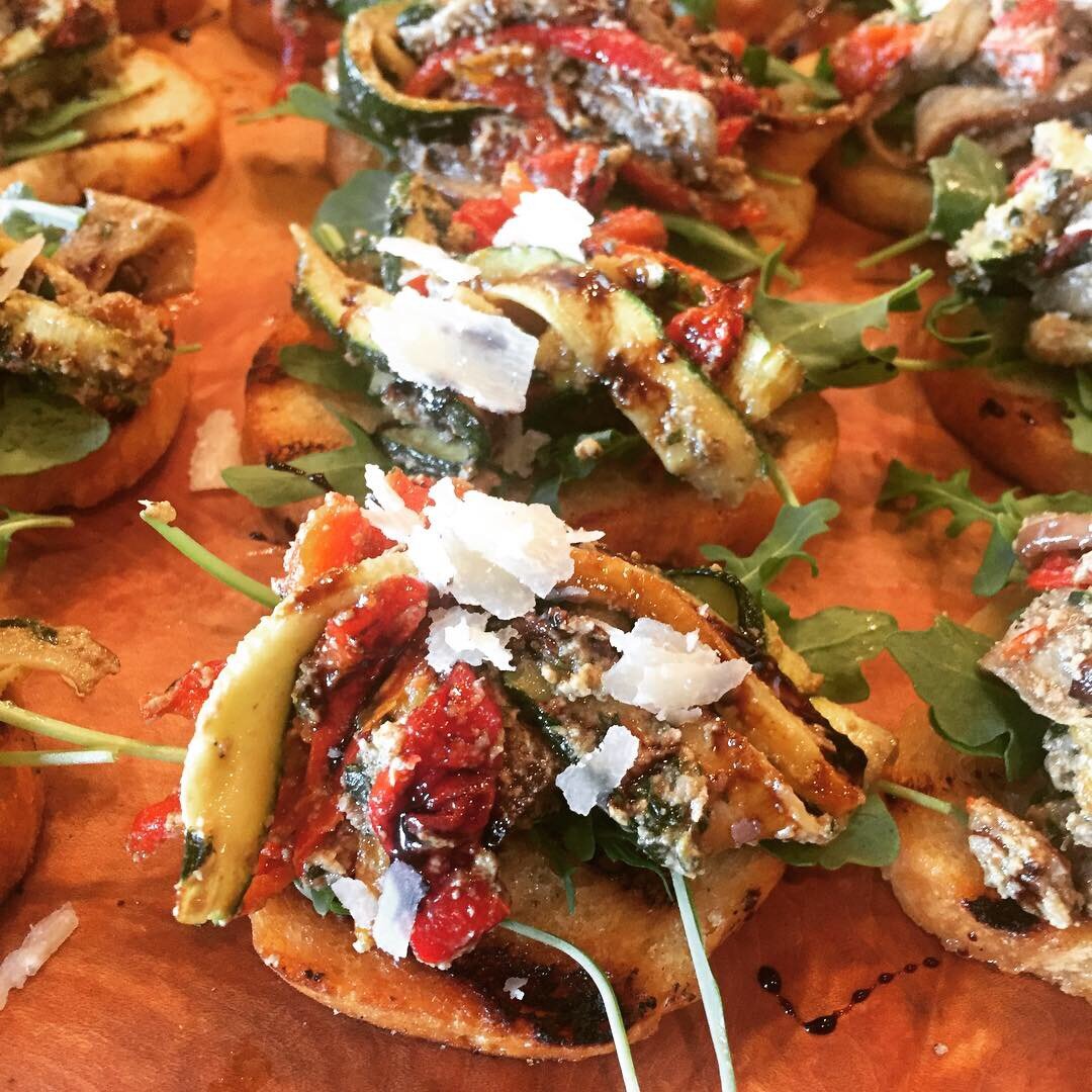 Colorful appetizer featuring toasted bread topped with arugula, grilled zucchini, sun-dried tomatoes, and a sprinkle of cheese, garnished for a gourmet presentation. Perfect for parties or as a healthy snack option.