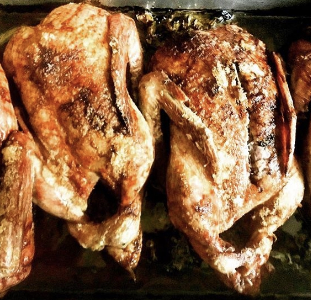 Two perfectly roasted whole chickens with crispy skin, arranged side by side on a baking tray, showcasing a golden-brown finish and juicy texture. Ideal for holiday meals or family gatherings.